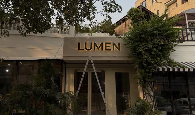 Illuminated LUMEN letters above a shop entrance, with a ladder still in front of the doors.