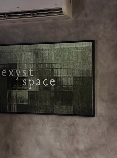Framed wall piece reading exyst space on a grey plaster wall.