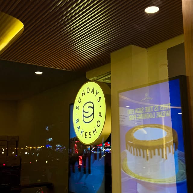 Round illuminated Sundays Bakeshop blade sign in a shop window at night.